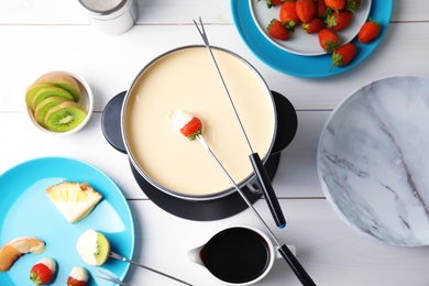 Flat lay composition with chocolate fondue in pot and fruits on wooden background