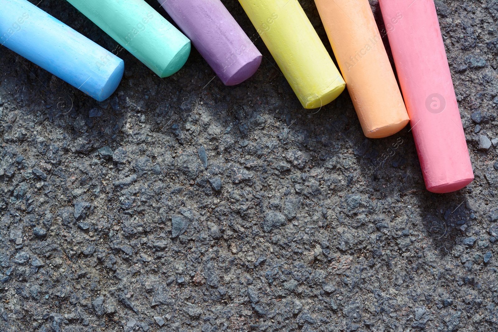 Photo of Colorful chalk sticks on asphalt, flat lay. Space for text