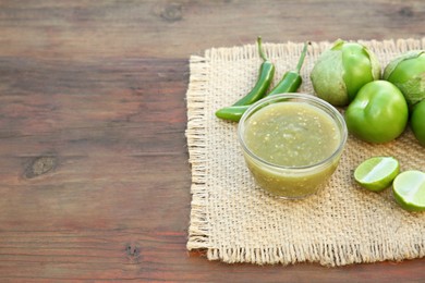 Photo of Tasty salsa sauce and ingredients on wooden table. Space for text