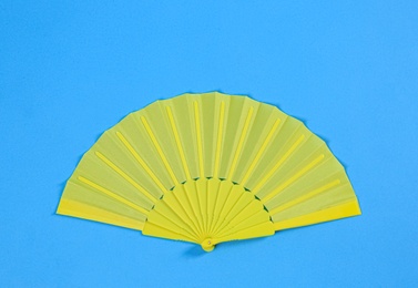 Yellow hand fan on light blue background, top view