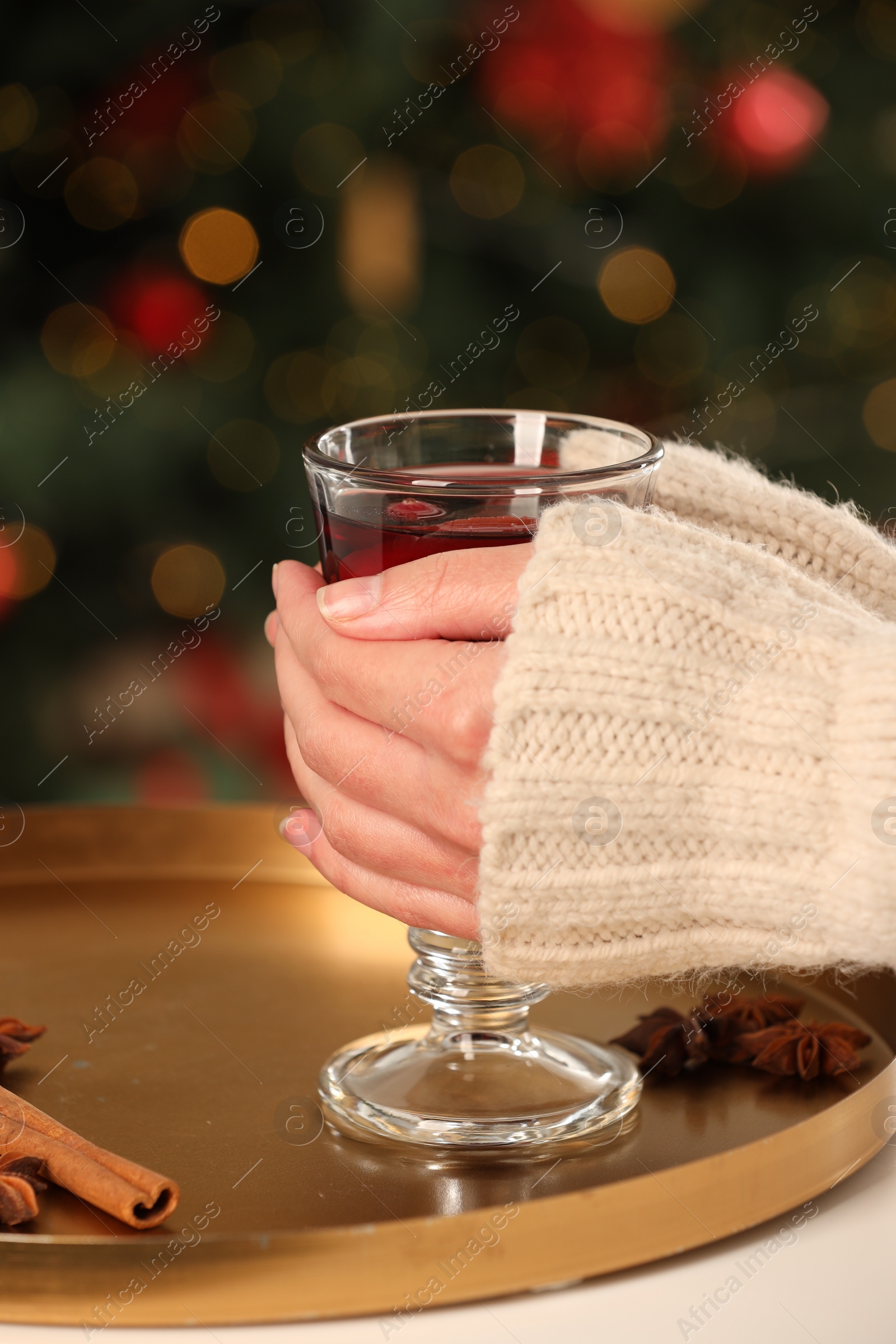 Photo of Woman holding glass cup of delicious mulled wine at white table against blurred background, closeup