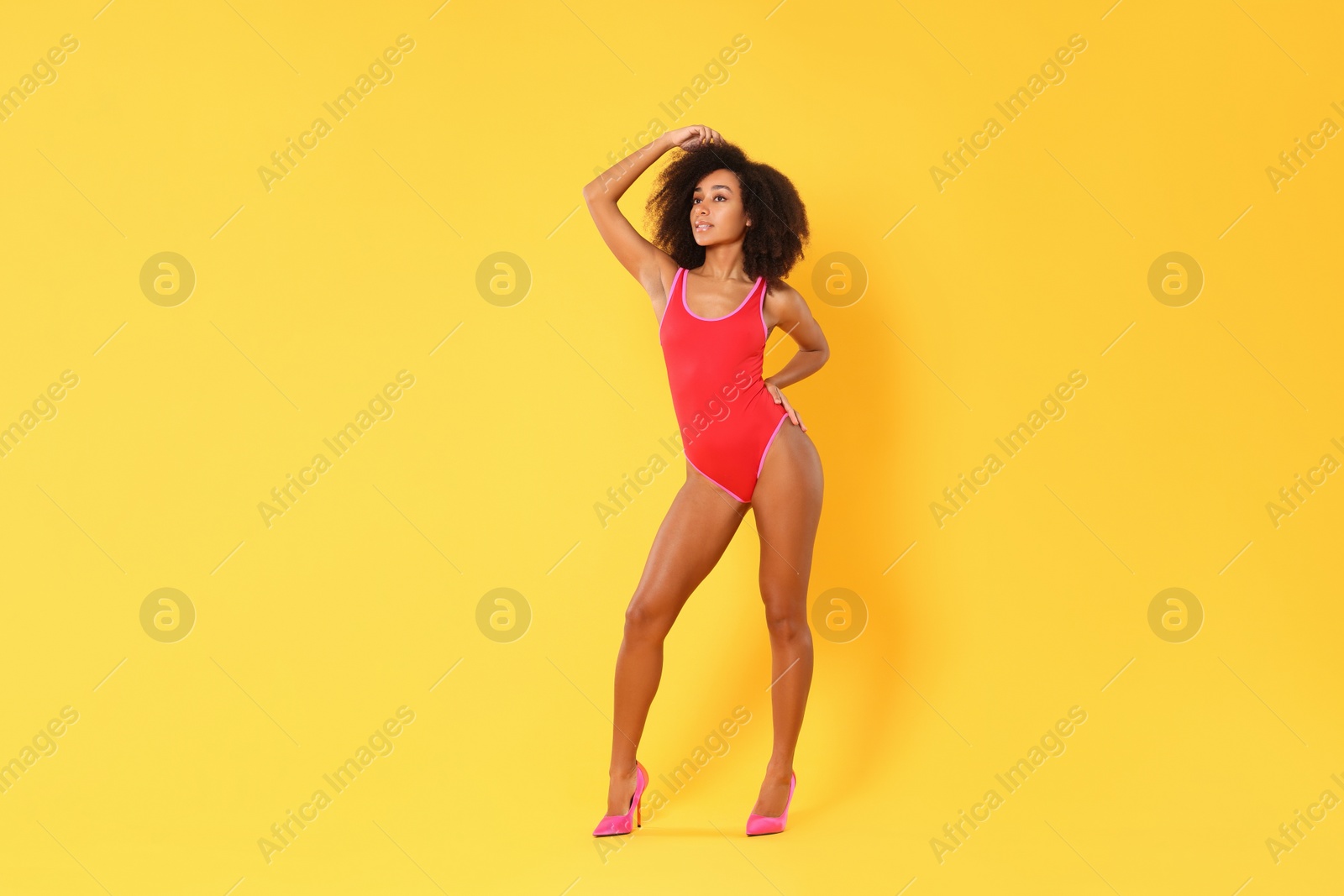 Photo of Beautiful woman in bright one-piece summer swimsuit and stylish high heel shoes on yellow background