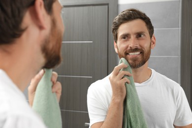 Photo of Handsome man drying his beard in front of mirror in bathroom