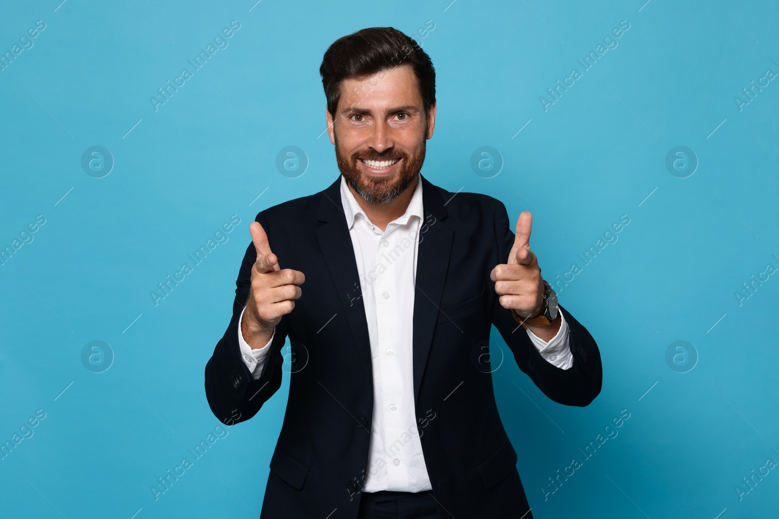 Photo of Smiling bearded man pointing forward index fingers on light blue background. Space for text