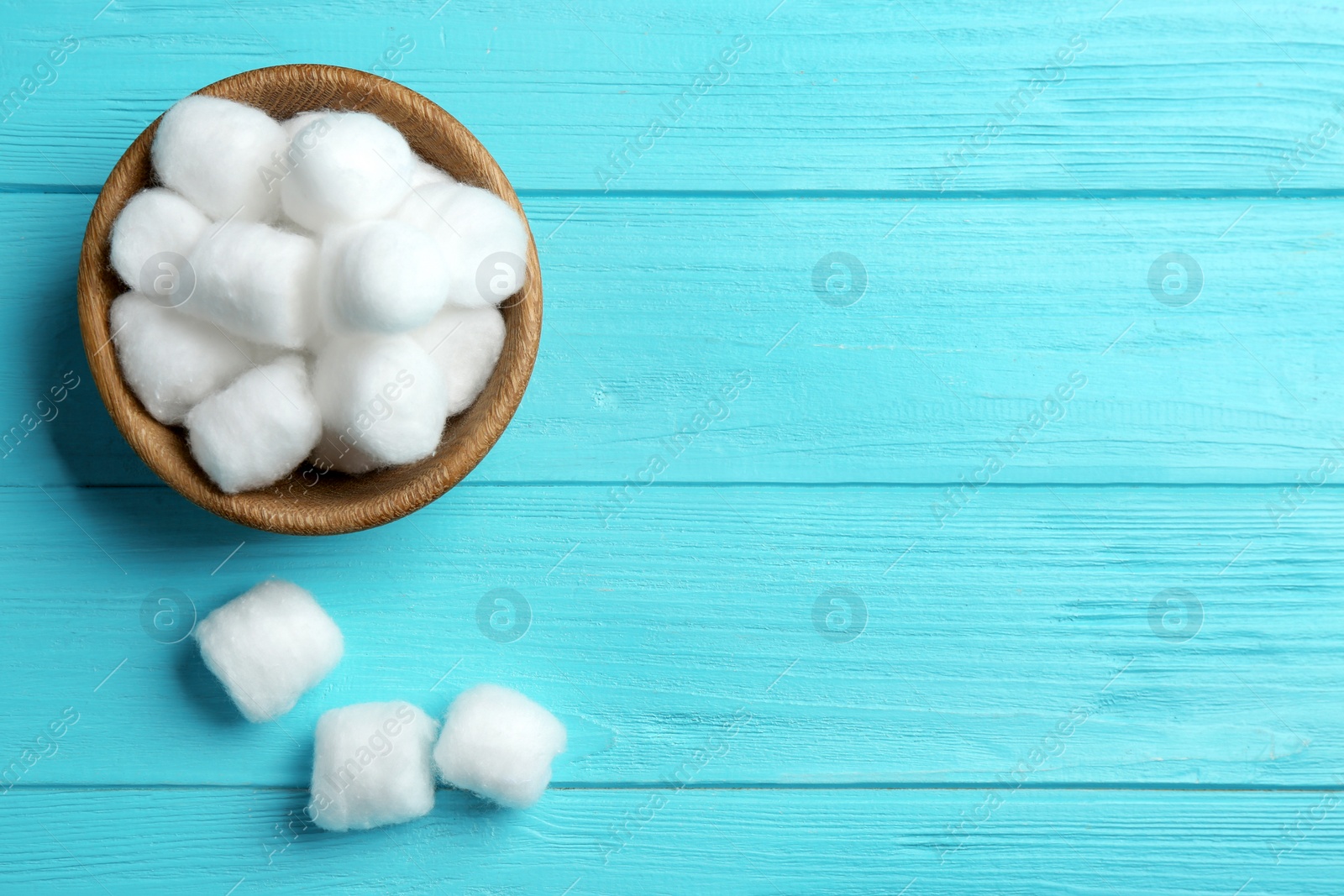 Photo of Bowl with fluffy cotton balls and space for text on color wooden background, flat lay