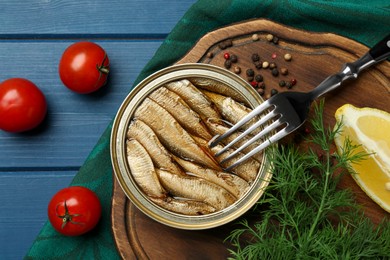 Photo of Tin can with tasty sprats served on blue wooden table, flat lay