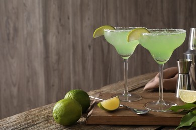 Photo of Delicious Margarita cocktail in glasses, limes and bartender equipment on wooden table, space for text
