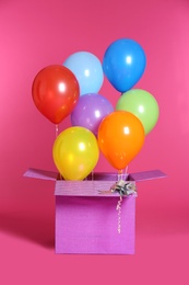 Gift box with bright air balloons on color background