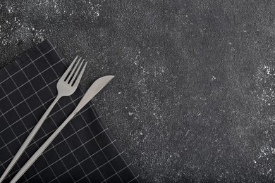 Shiny fork, knife and napkin on black table, flat lay. Space for text