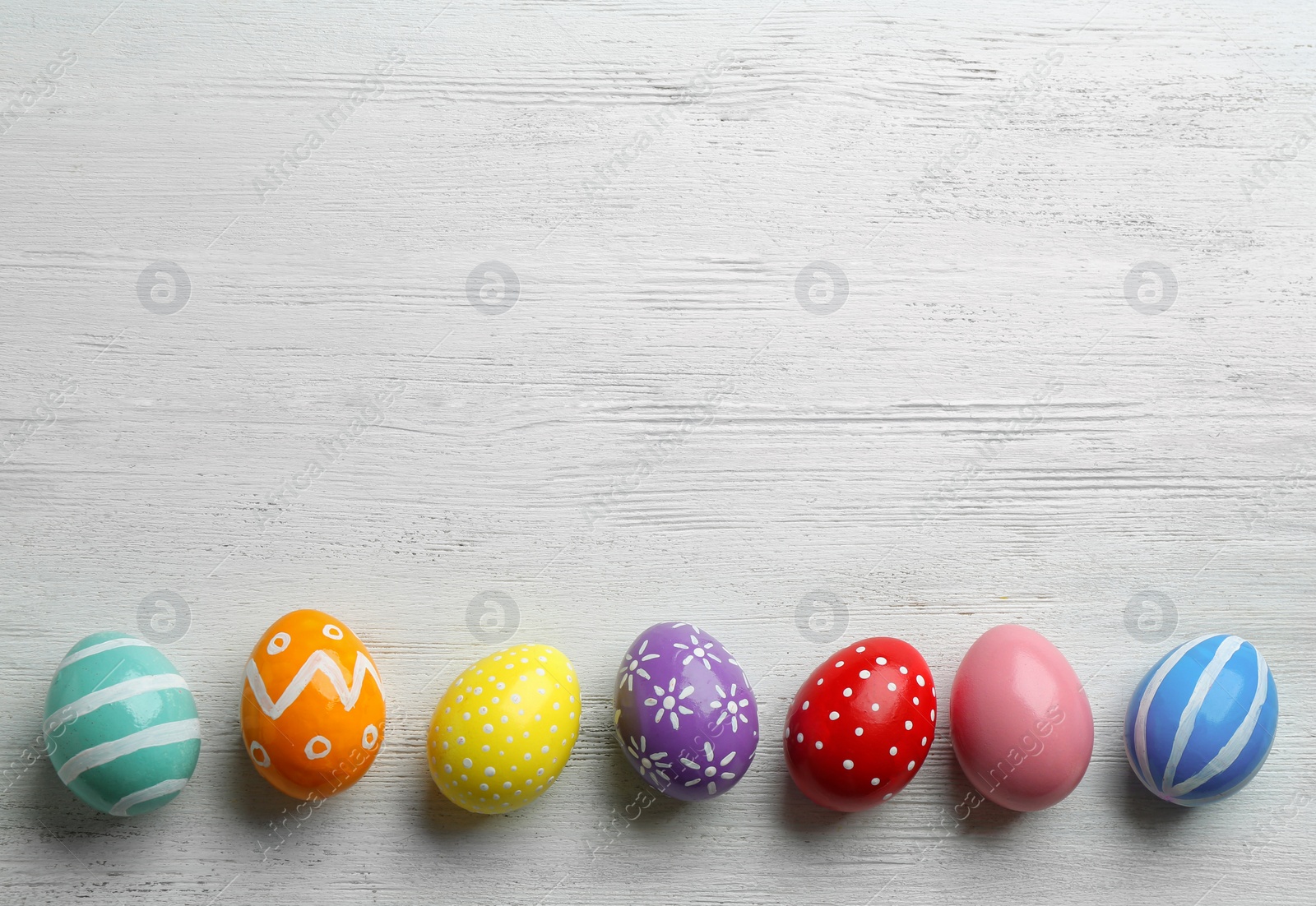 Photo of Flat lay composition of painted Easter eggs on wooden table, space for text