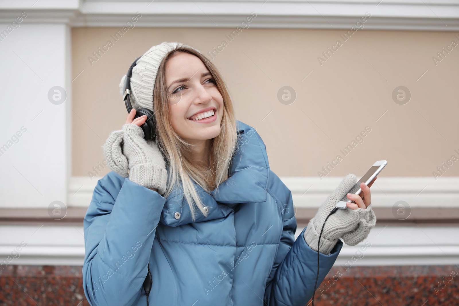 Photo of Young woman with headphones listening to music near light wall