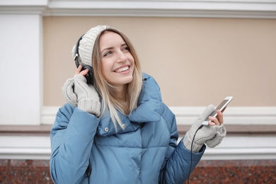 Young woman with headphones listening to music near light wall