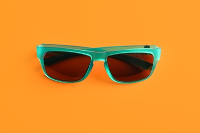 Stylish sunglasses on orange background, top view