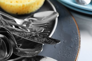 Photo of Plates with silverware and sponge in water drops, closeup