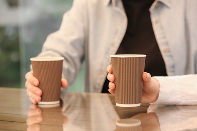 Women holding takeaway paper cups at table, closeup. Coffee to go