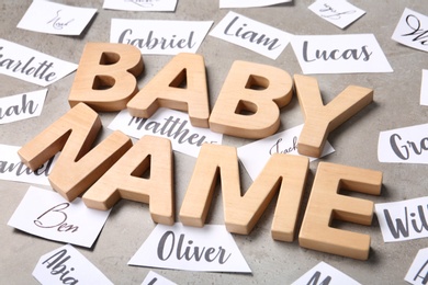 Photo of Paper sheets with different baby names, and wooden letters on grey background, closeup