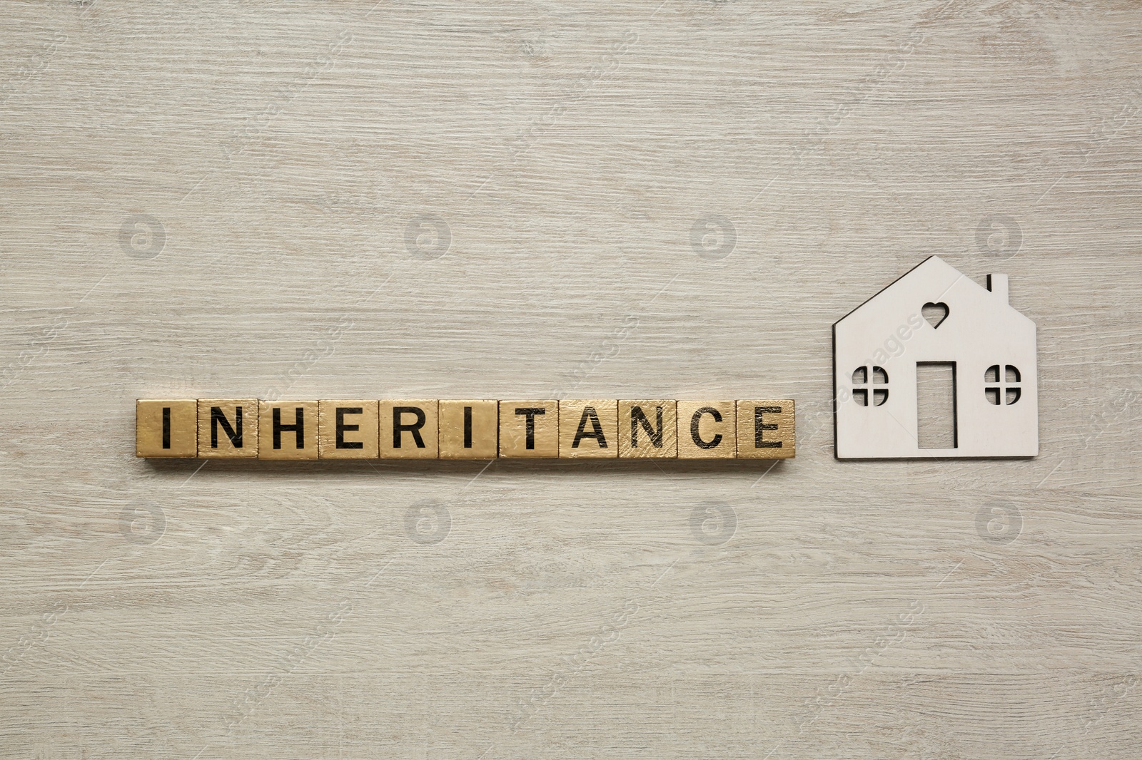 Photo of Word Inheritance made with cubes and house model on light wooden background, flat lay
