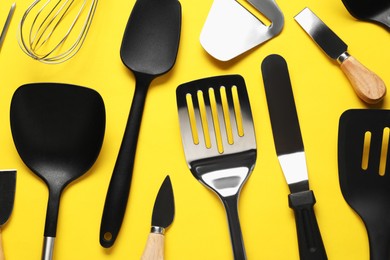 Photo of Different spatulas and other kitchen utensils on yellow background, flat lay