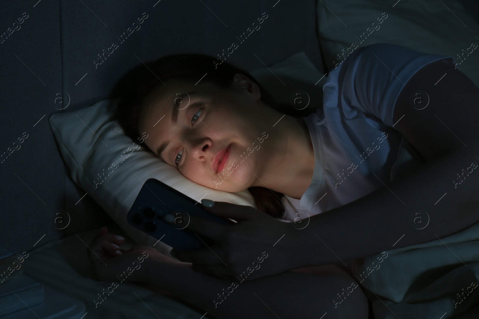 Photo of Woman using smartphone on bed at night. Internet addiction