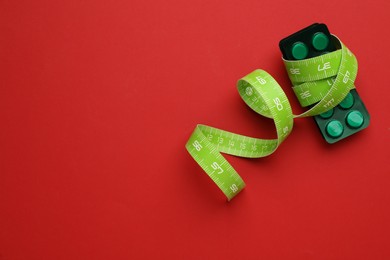 Photo of Weight loss pills and measuring tape on red background, top view. Space for text
