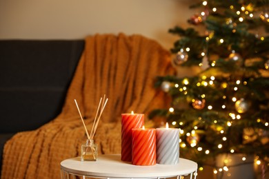 Photo of Beautiful candles and reed air freshener near Christmas tree indoors. Cosy atmosphere