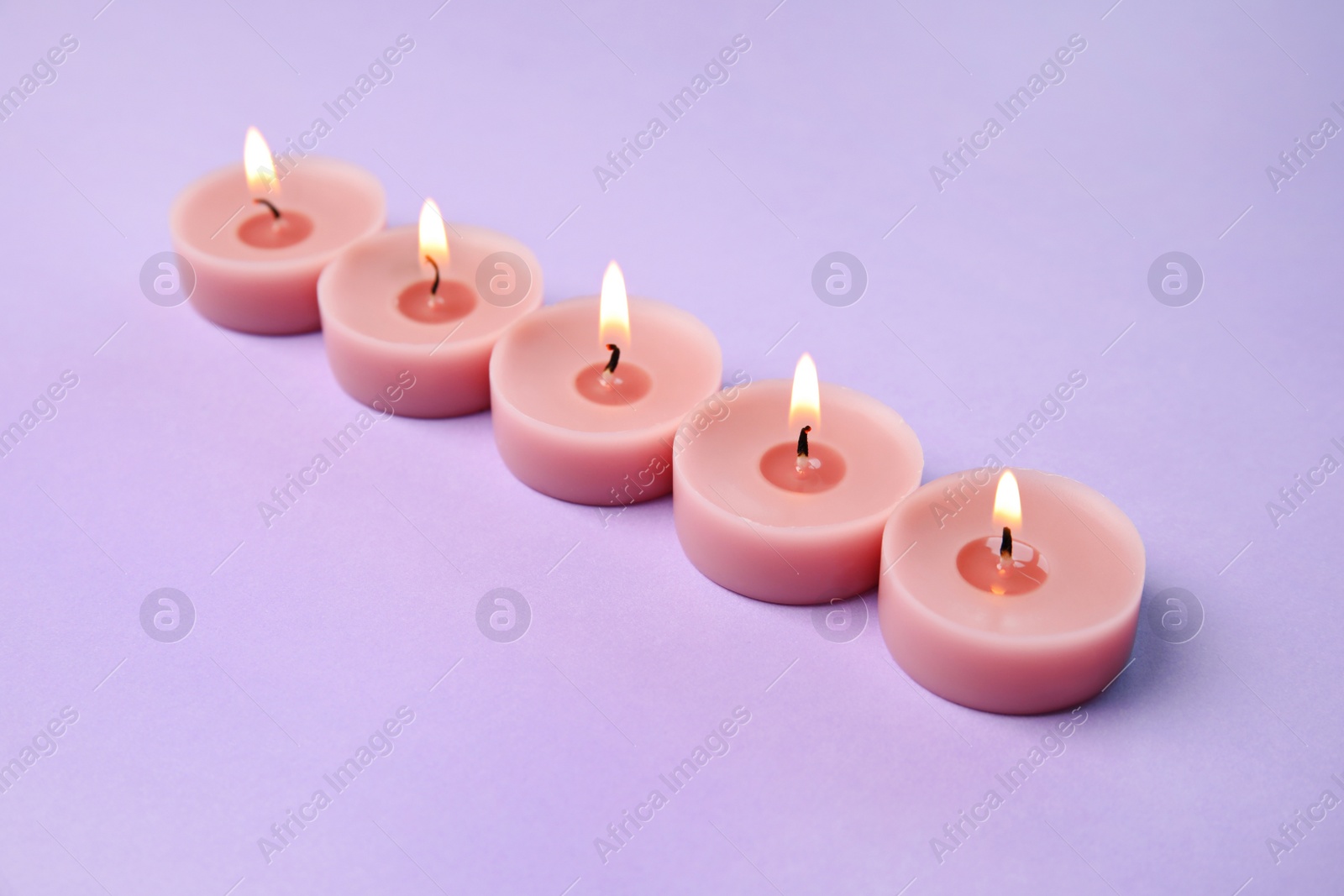 Photo of Burning wax decorative candles on purple background