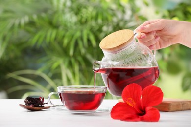 Woman pouring delicious hibiscus tea into cup at white wooden table outdoors, closeup