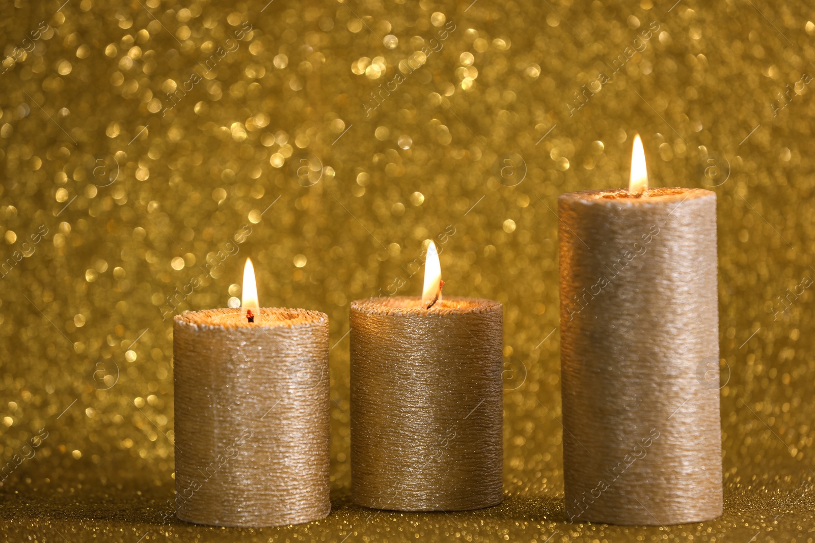 Photo of Burning candles on gold shining background, space for text