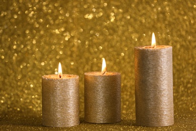 Photo of Burning candles on gold shining background, space for text