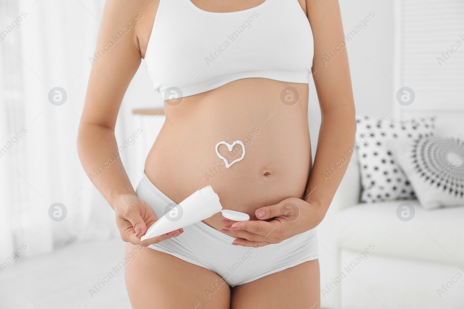 Photo of Heart painted with body cream on pregnant woman's belly at home, closeup