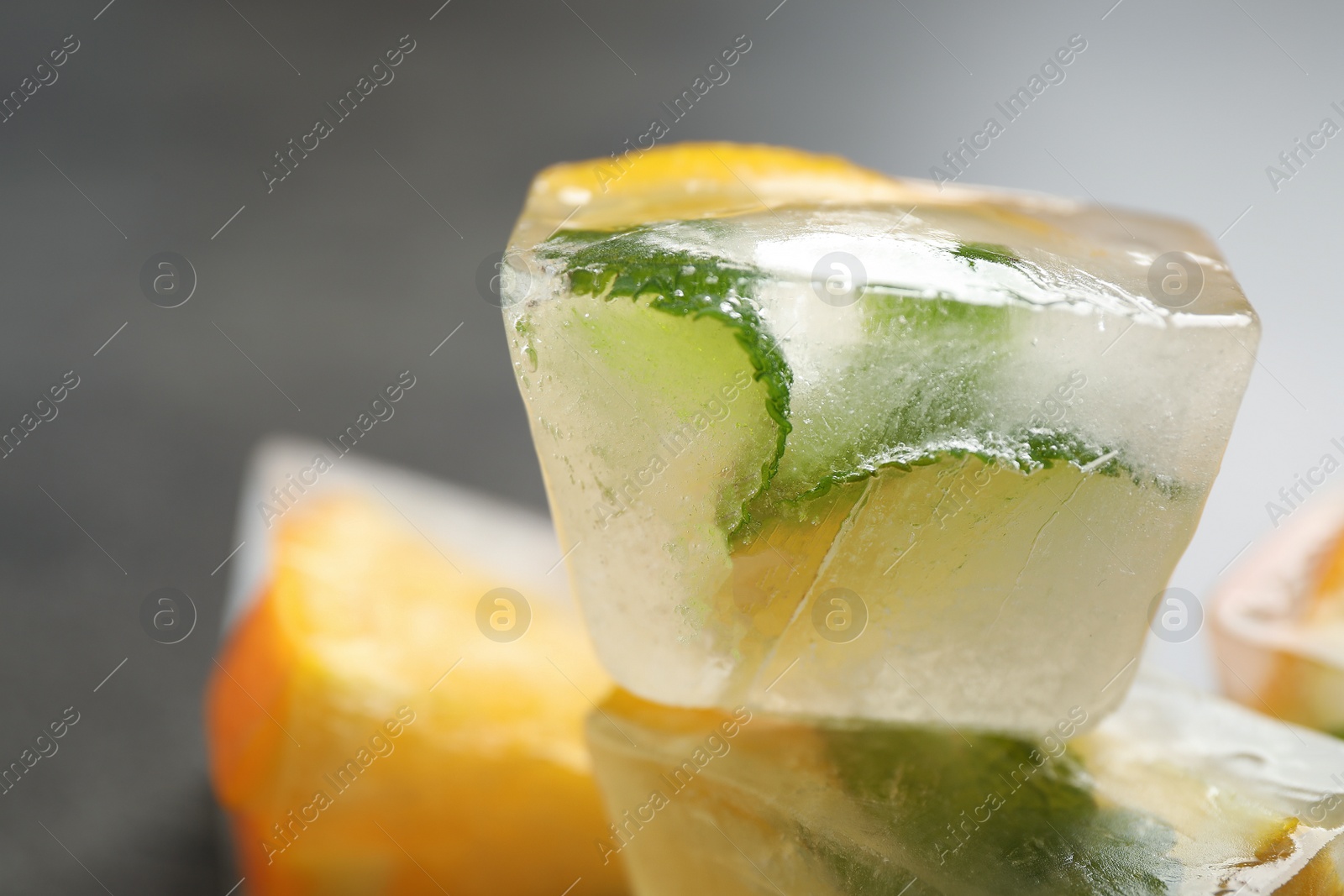 Photo of Ice cubes with orange and mint on grey table, closeup