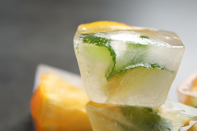 Photo of Ice cubes with orange and mint on grey table, closeup