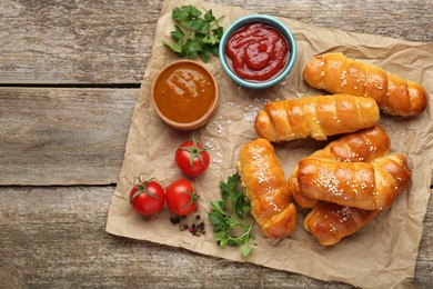 Photo of Delicious sausage rolls and ingredients on wooden table, top view. Space for text