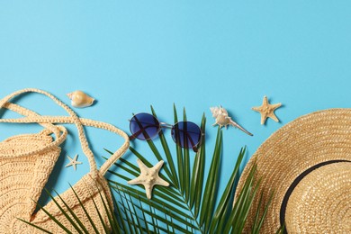 Photo of Flat lay composition with wicker bag, palm leaves and other beach accessories on light blue background. Space for text
