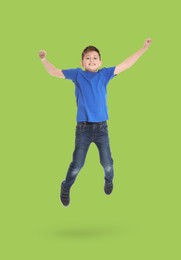 Happy boy jumping on light green background, full length portrait