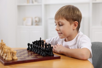 Cute little boy playing chess at table in room