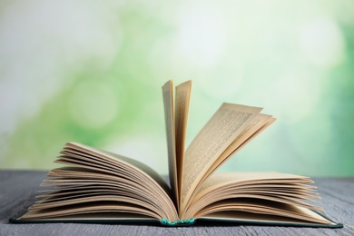 Photo of Open book on grey wooden table against blurred green background
