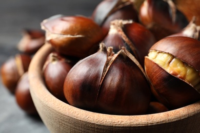 Photo of Delicious roasted edible chestnuts in wooden bowl on table, closeup