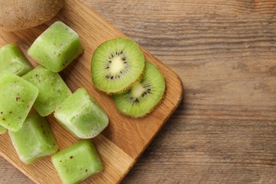 Photo of Frozen kiwi puree cubes and ingredient on wooden table, top view. Space for text