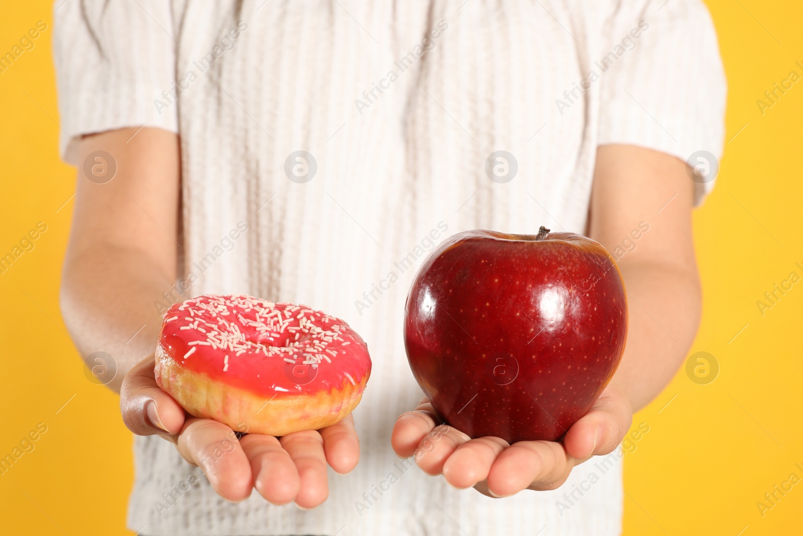 Photo of Concept of choice. Woman holding apple and doughnut on yellow background, closeup