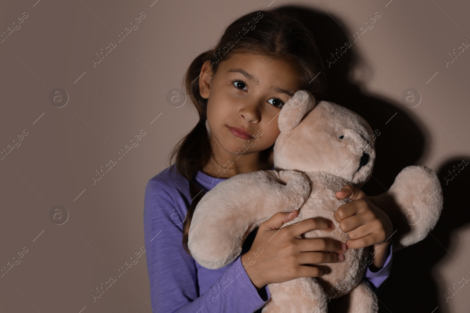 Photo of Sad little girl with teddy bear near beige wall. Domestic violence concept