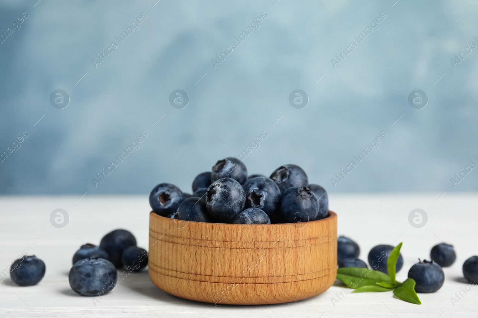 Photo of Fresh ripe blueberries in bowl on white wooden table