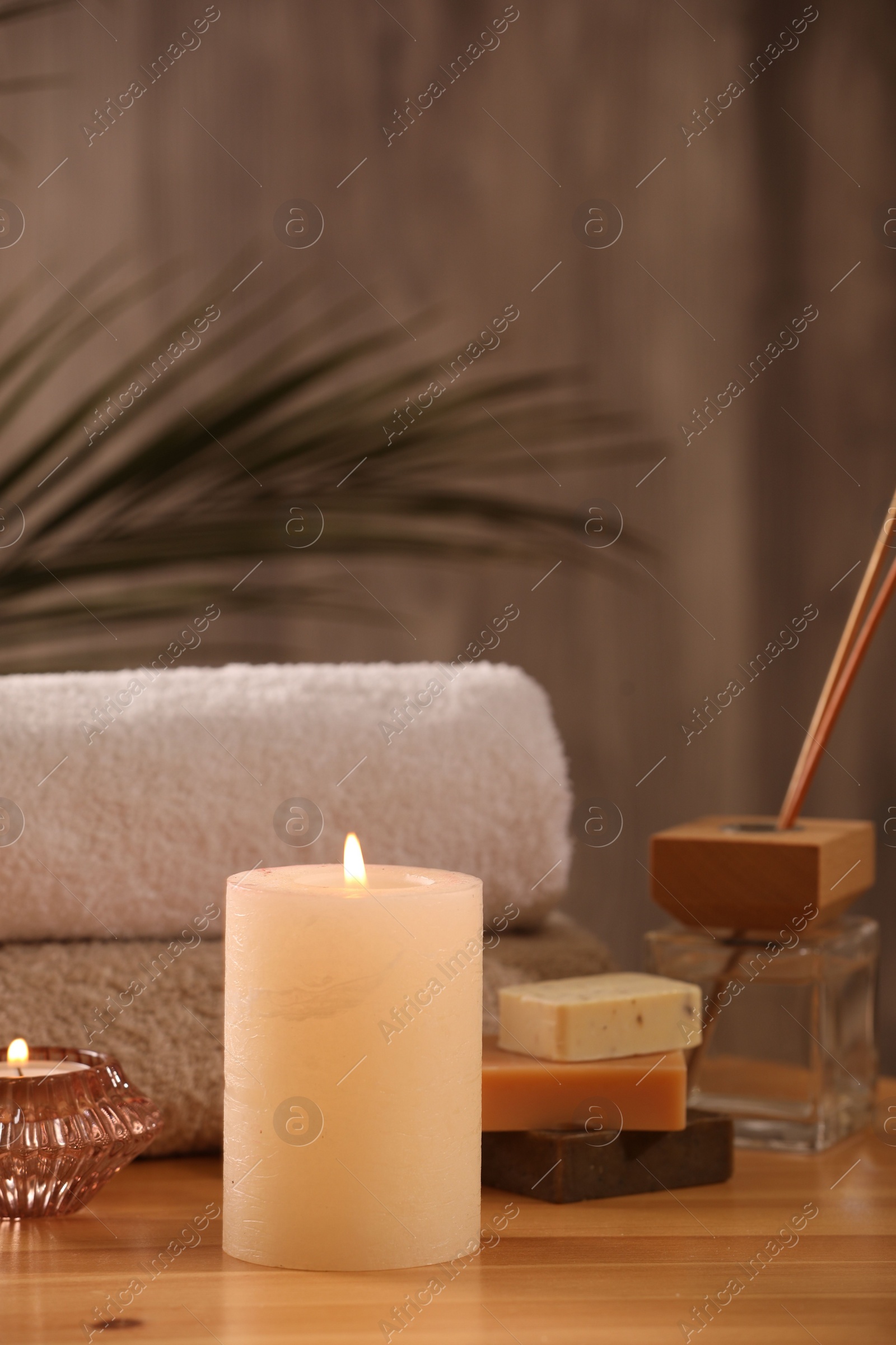 Photo of Spa composition. Burning candles, towels, soap and reed air freshener on wooden table, closeup