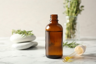 Composition with bottle of rosemary oil and fresh twigs on light table