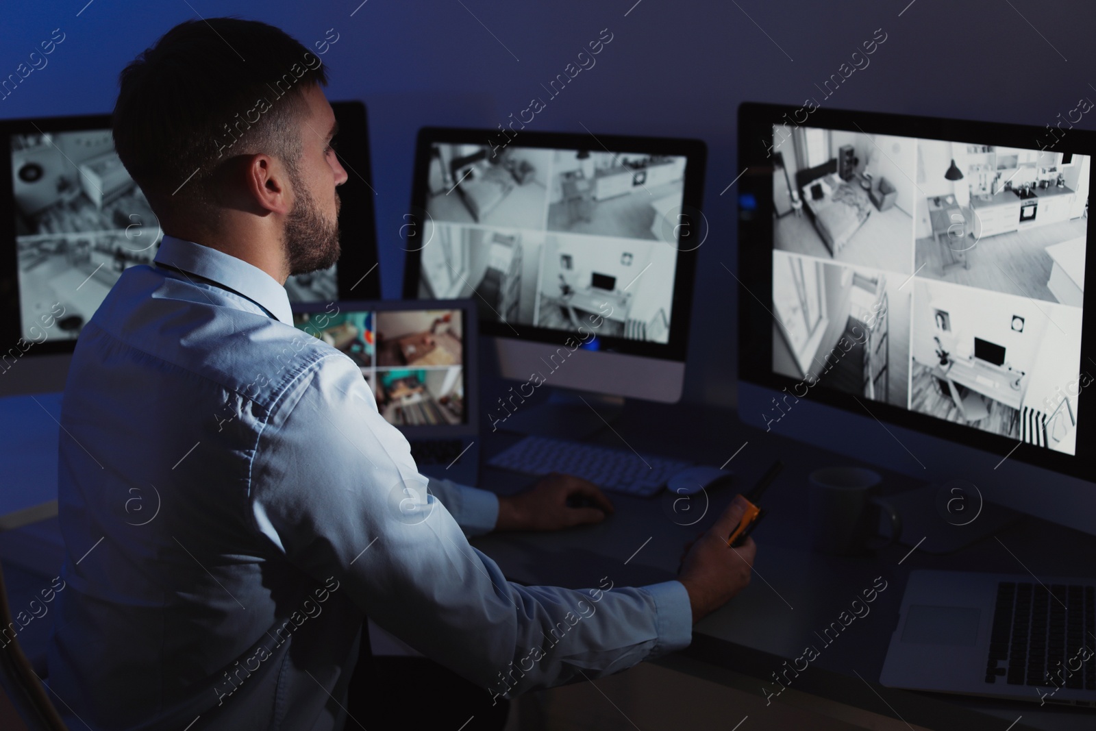 Photo of Male security guard with portable transmitter monitoring home cameras indoors at night