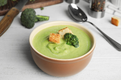 Photo of Delicious broccoli cream soup with croutons served on white wooden table