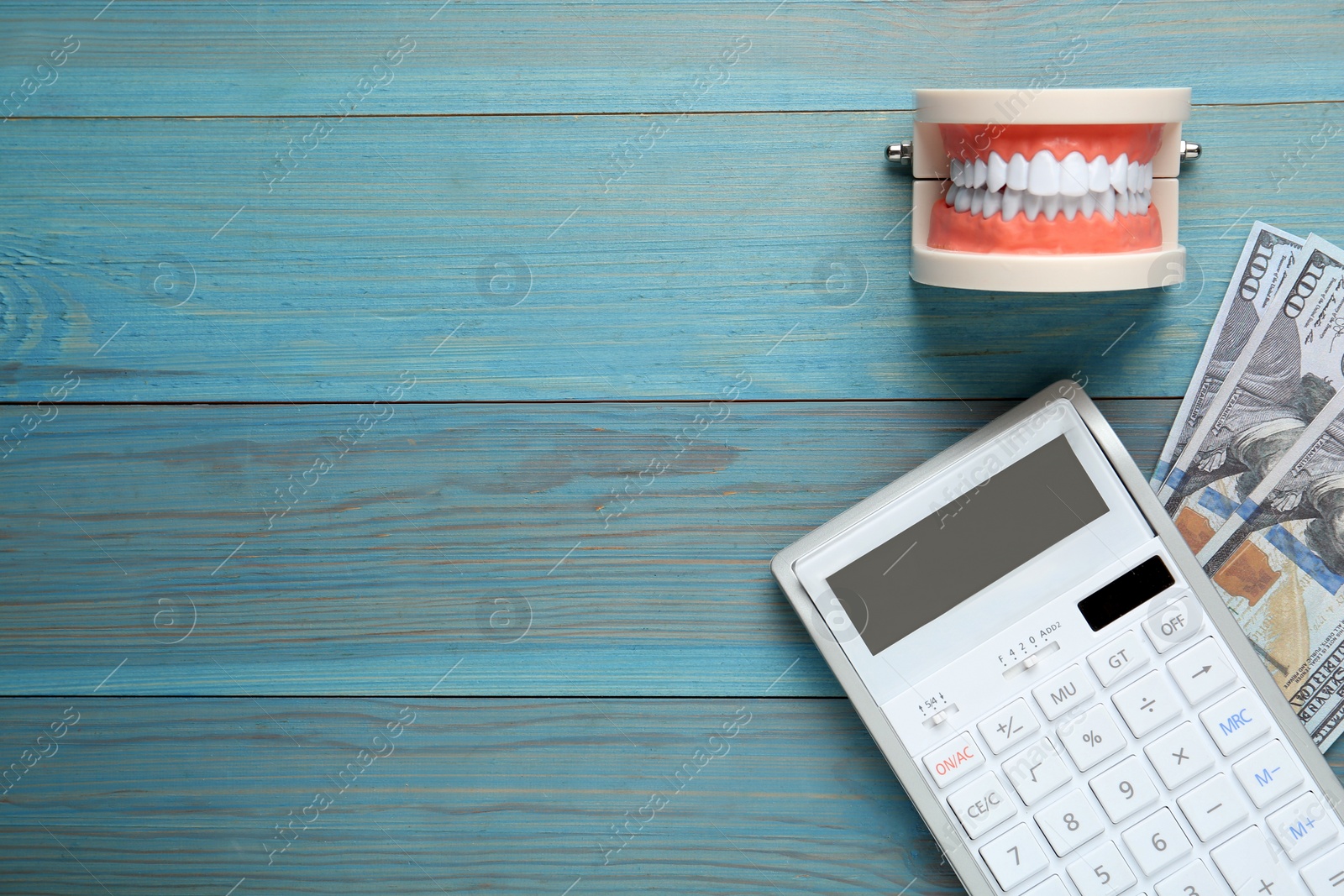 Photo of Educational dental typodont model, dollar banknotes and calculator on light blue wooden table, flat lay with space for text. Expensive treatment