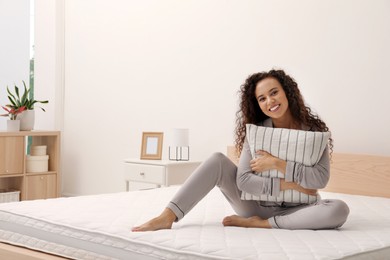 Photo of Happy young African American woman hugging pillow on bed with comfortable mattress at home