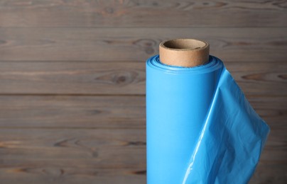 Photo of Roll of plastic stretch wrap film on wooden background, closeup. Space for text