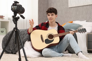 Photo of Smiling teenage blogger with guitar recording video tutorial at home